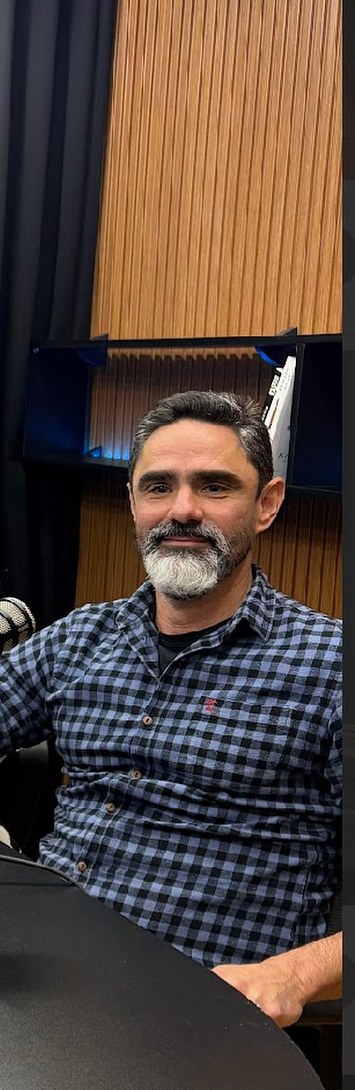 Dr. Ivo Pinfildi sentado à mesa de gravação, com microfone e painel de madeira ripada ao fundo